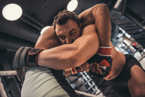 Two men in boxing gloves and shorts are fighting in cage using grappling technique